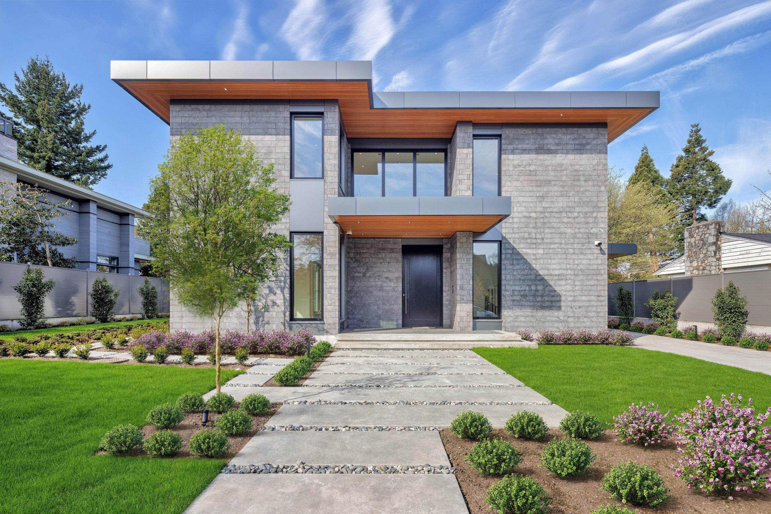 Contemporary two-story house in Vancouver, BC, featuring a gray brick exterior, large windows, and a landscaped front yard—showcasing quality construction.