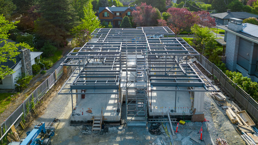 Aerial view of a house under construction with exposed steel framework, surrounded by trees. Built by a BC general contractor.