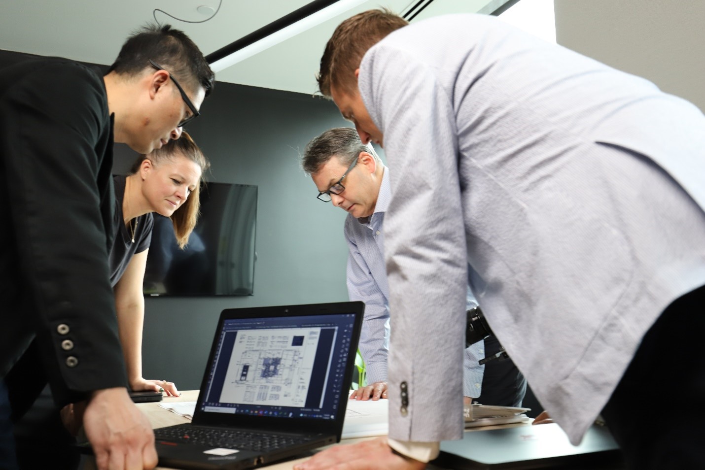 Four people lean over a table, discussing construction plans displayed on a laptop in an office in British Columbia.