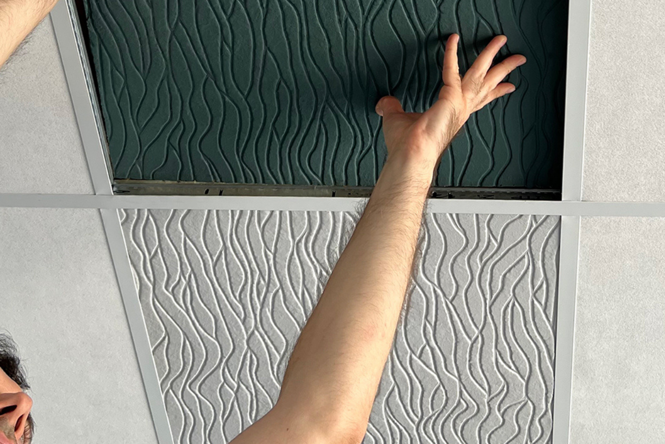 A person’s arm reaches up to open a tile in a patterned ceiling.