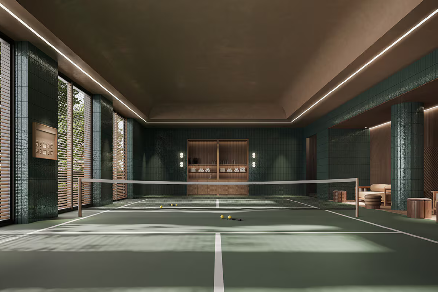 A modern indoor tennis court with green tiles, tennis equipment, and seating area in the background.