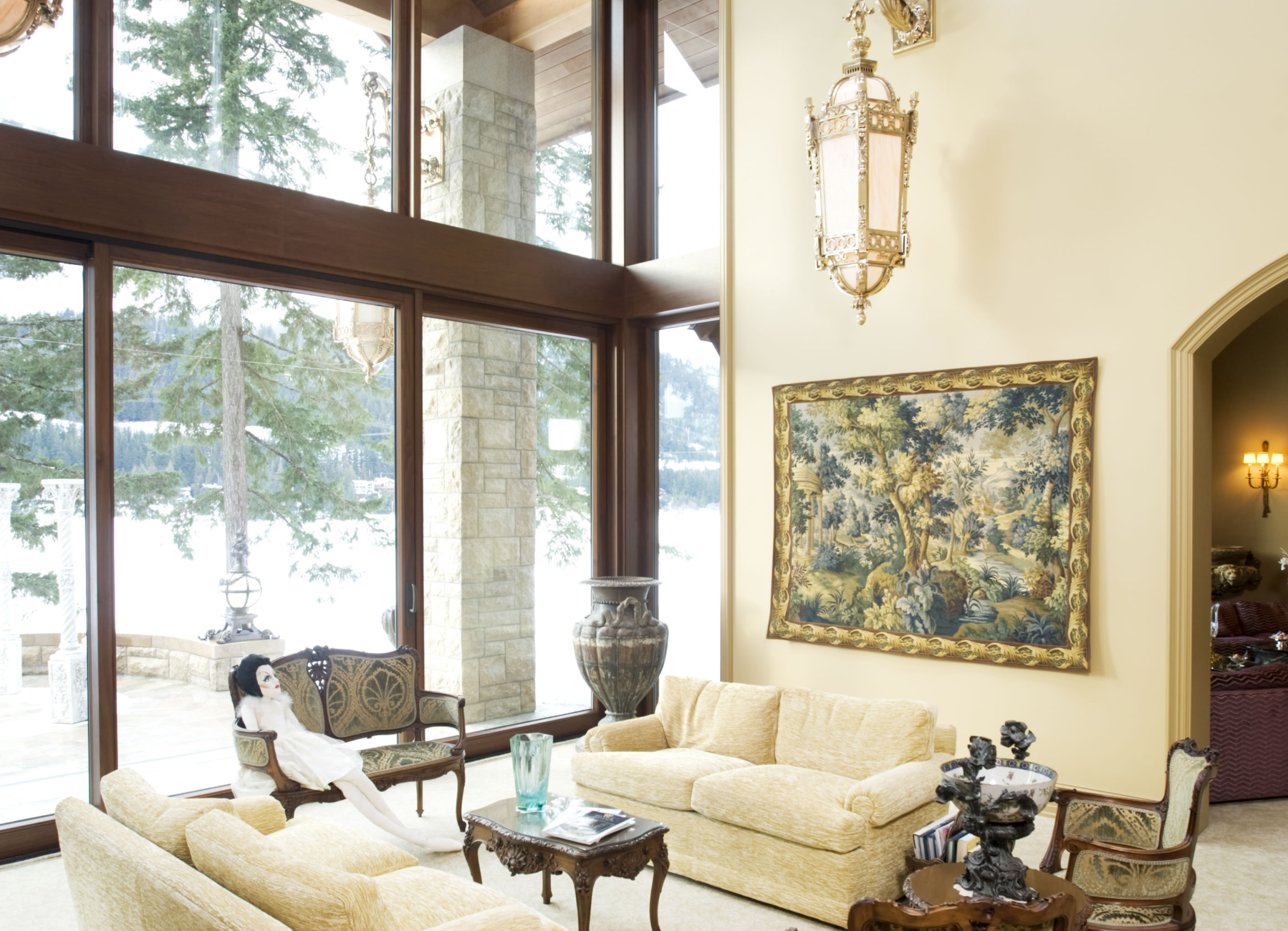 Sunlit living room with cream sofas, carved wood chairs, a large framed tapestry on the wall, and an ornate hanging lantern near the window.