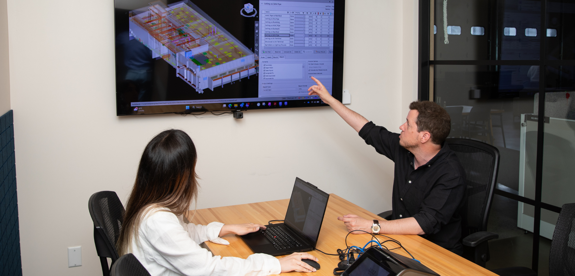 BIM team members reviewing a 3D building model on a large screen, discussing construction coordination and design details.